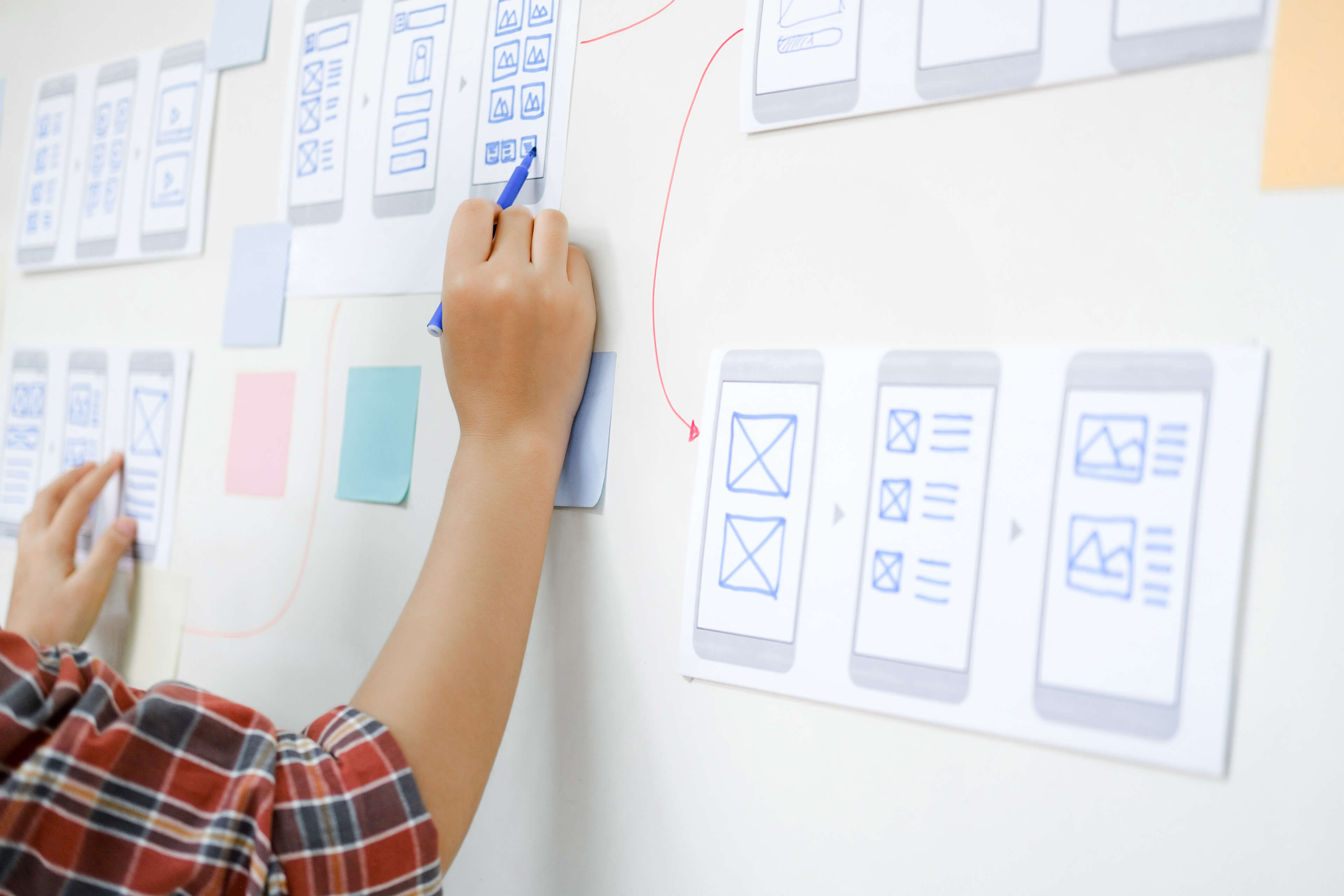 Photograph of mobile user interface designs on a wall being edited and examined for user experience